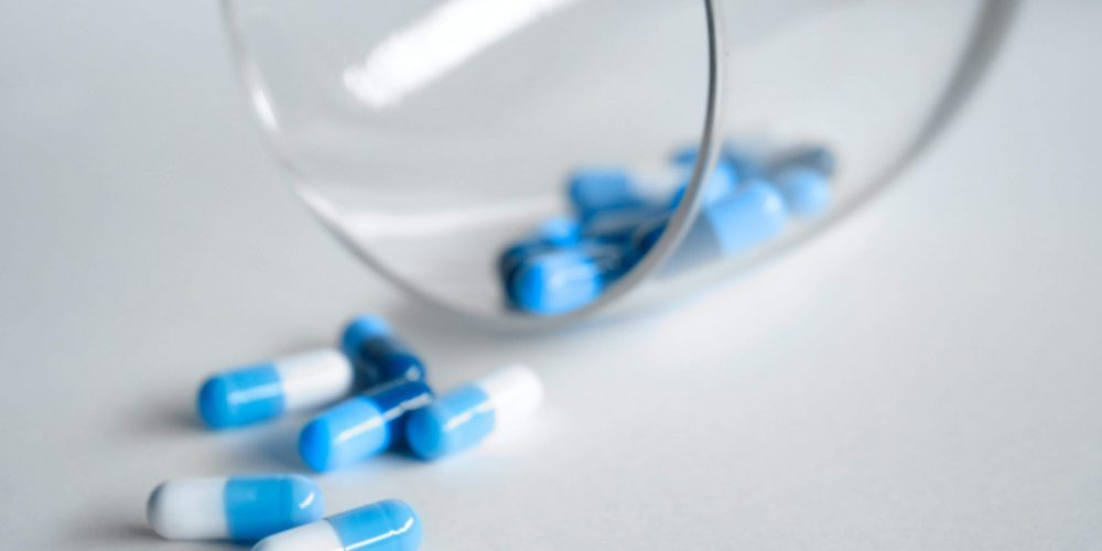 viser nogle blå piller, der er hældt ud af et glas - Medicinmisbrug, Medicinafhængighed & Benzodiazepiner
